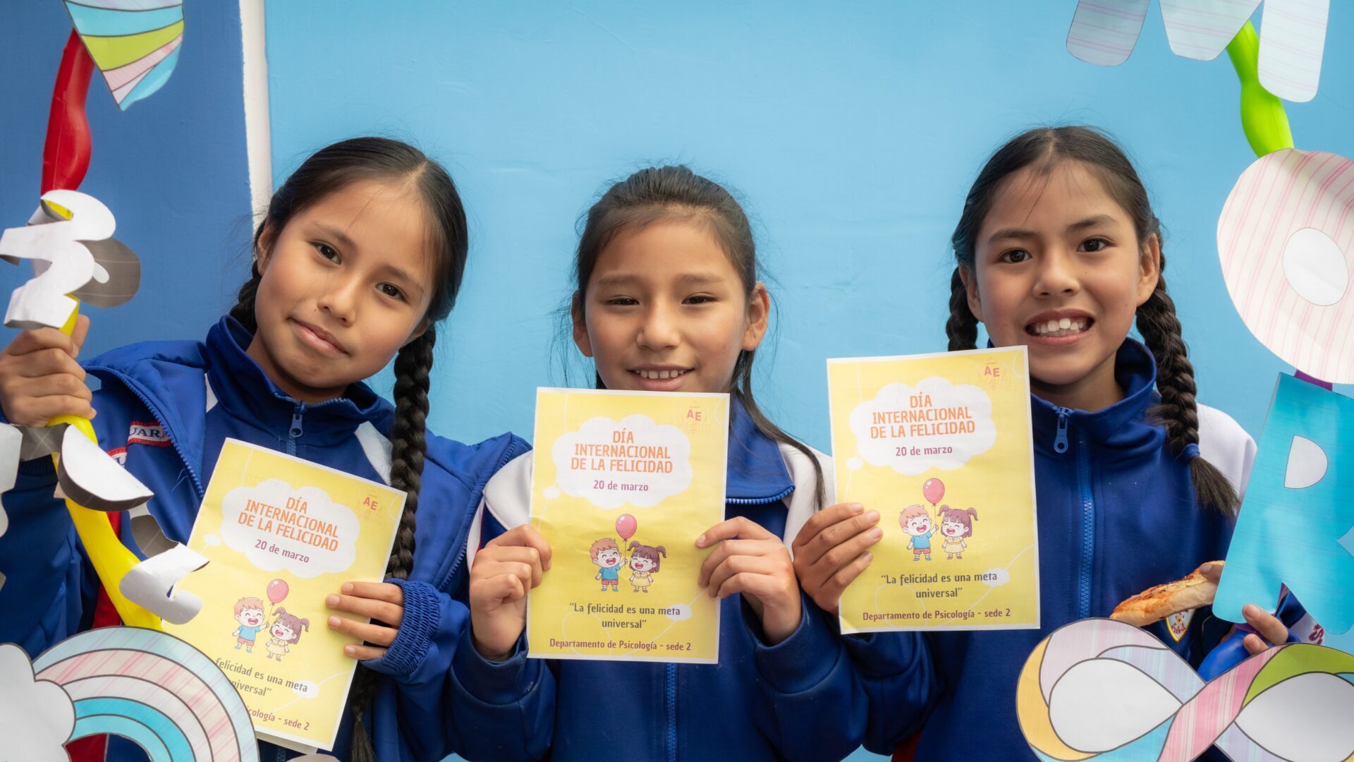 Tres alumnas del Colegio Albert Einstein muestran un díptico que conmemora el Día Internacional de la Felicidad